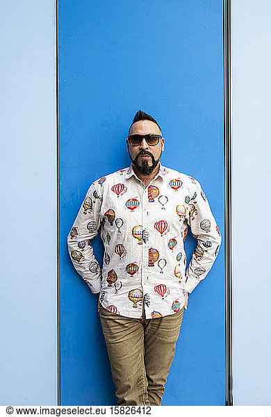 Bearded male leaning on colored wall with sunglasses  looking camera