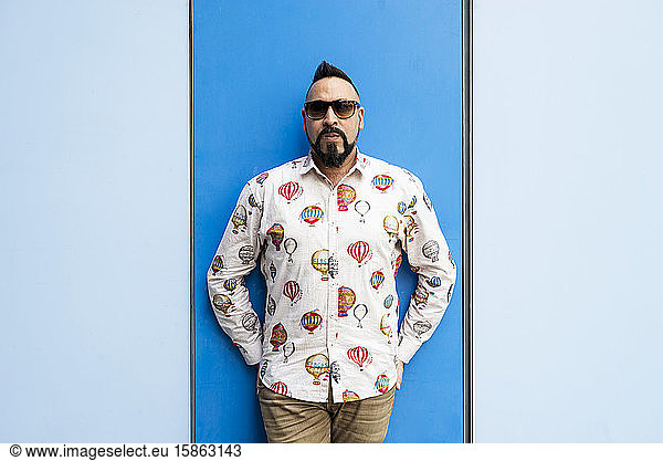 Bearded male leaning on colored wall with sunglasses  looking camera