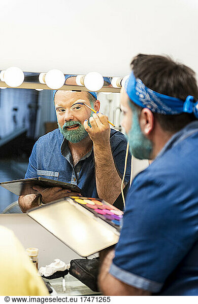 Bearded man applying eyeshadow in dressing room