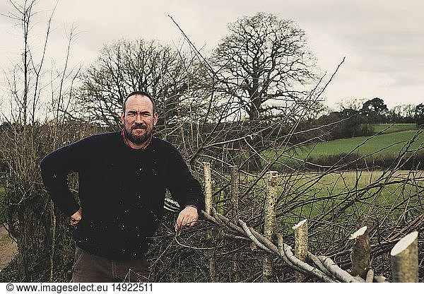 Bearded man standing next to a newly built traditional hedge  smiling at camera.