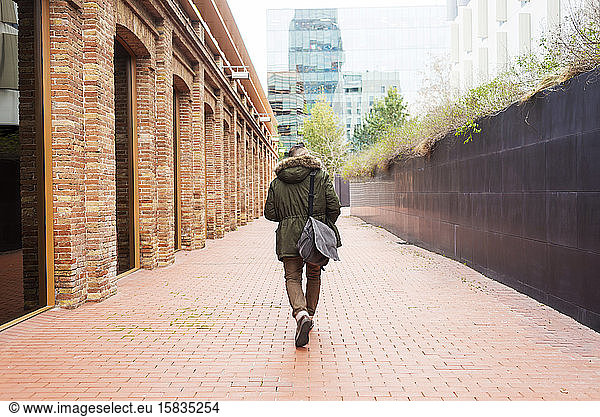 Bearded man walking across pathway holding a take away coffee
