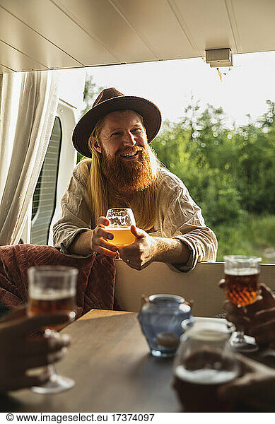 Bearded man with beer glass talking with friends in motor home