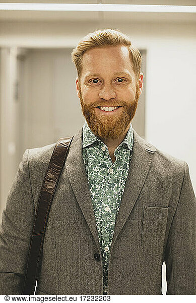 Bearded smiling businessman in corridor at office