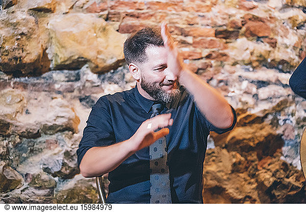 Bearded smiling singer clapping hands while singing against wall in club