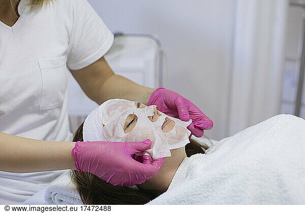 Beautician applying hydrating face mask to woman in salon