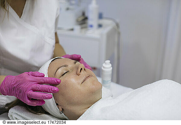 Beautician doing face massage of mature woman in salon