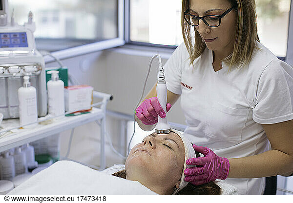 Beautician doing ultrasonic facial of mature woman with equipment in salon