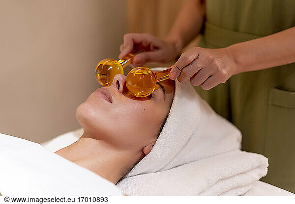 Beautician holding glass globes on female customer's face at health spa