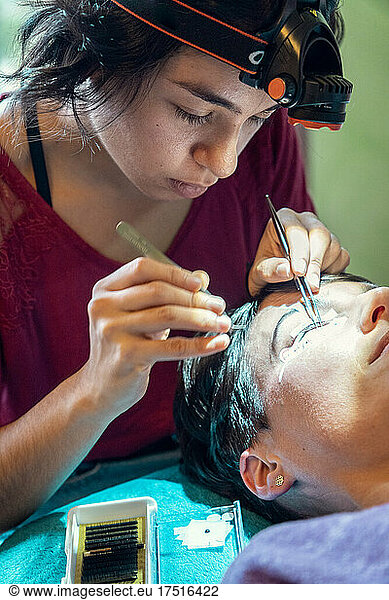 beautician placing false eyelashes to client at home