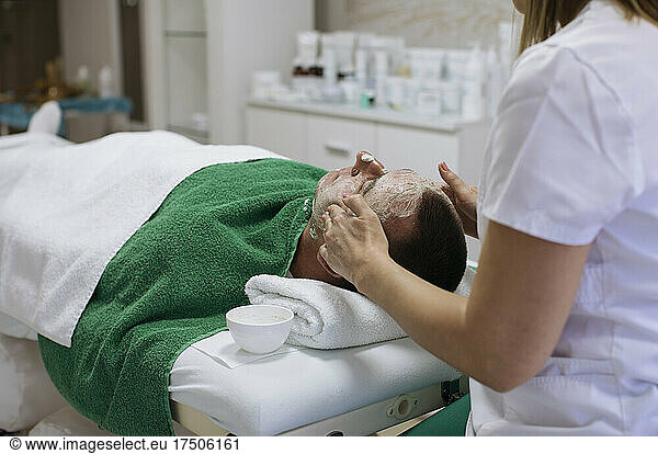 Beautician rubbing cream on customer's face in beauty spa