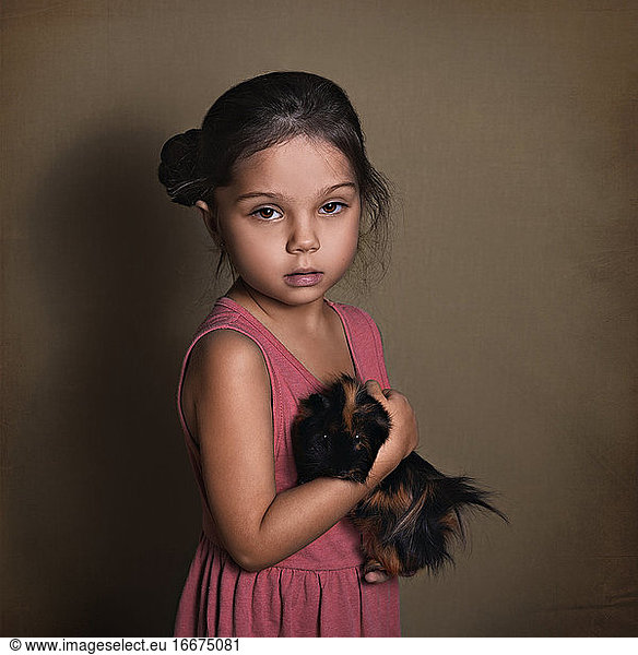 beautiful baby girl holding a fluffy Guinea pig on a paper background