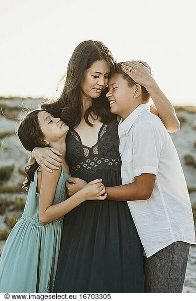 Beautiful dark-haired mom embracing young daughter and preteen son