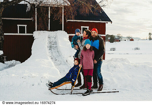 Beautiful family standing by red barn in Norwegian countryside in snow