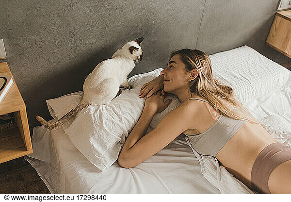beautiful girl lies on the bed and plays with a pet cat