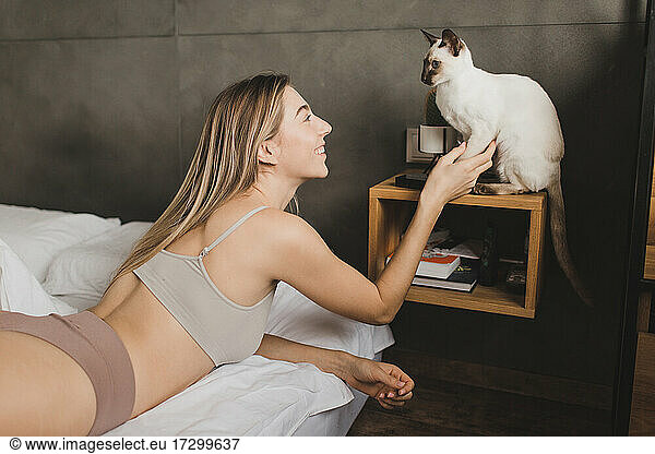beautiful girl lies on the bed and plays with a pet cat