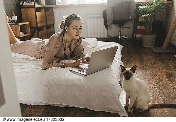 beautiful girl lies on the bed with a laptop and studies makes notes