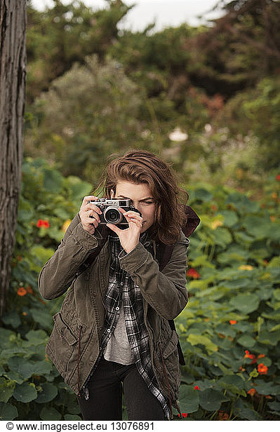 Beautiful hiker photographing through old-fashioned camera in forest
