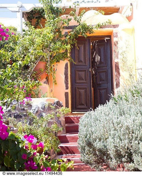 Beautiful solid brown door with stairs and flowers all around. Typical house entrance of the village of Pyros. Pyrgos was built on the top of a hill and was until the early 1800  the capital of the island. The village is composed of traditional houses built around the Venetian Castle and the small streets follow the shape of the hill. Climing from the square up to the castle of The village has many churches  but the most famous is the Monastery of Profitis Ilias  where a small collection of ethnographic material and old icons are exhibits.