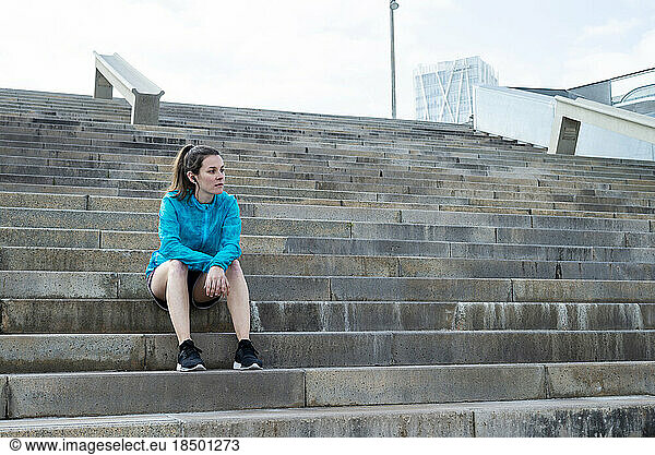 Beautiful sports woman sitting on stairs while looking away