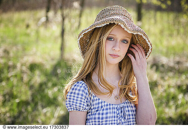 Beautiful teen blond girl outdoors in sundress and sun hat  backlit.