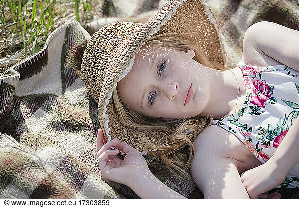 Beautiful Teen Girl with sun hat lying on a blanket outdoors.