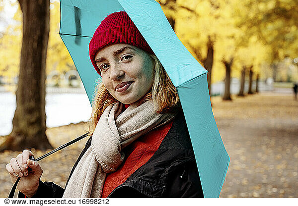 Beautiful teenage girl holding umbrella while standing at park