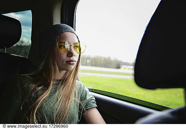 Beautiful tween girl with long blond hair and sunglasses in car.
