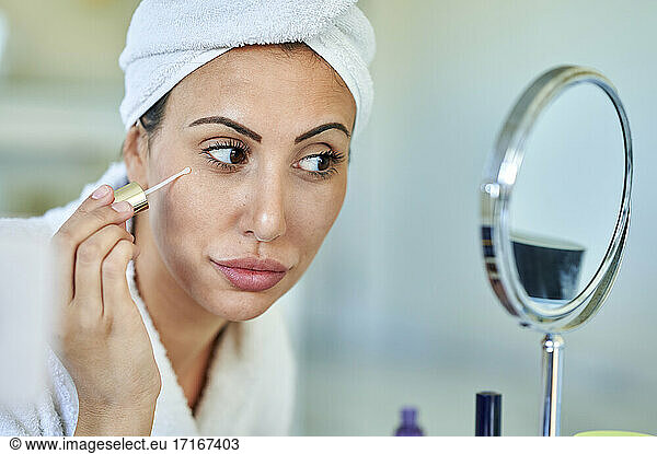 Beautiful woman applying beauty serum while looking in mirror at home