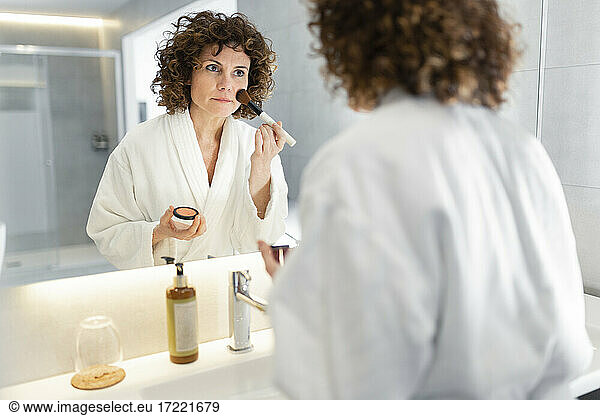 Beautiful woman applying powder from make-up brush in bathroom