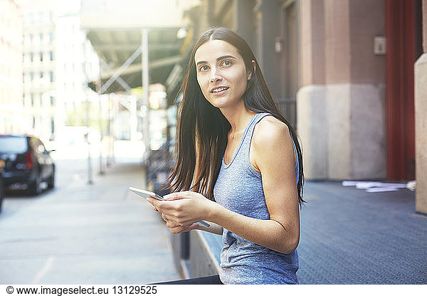 Beautiful woman holding digital tablet and sitting on retaining wall