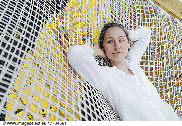 Beautiful woman resting with hands behind head on hammock