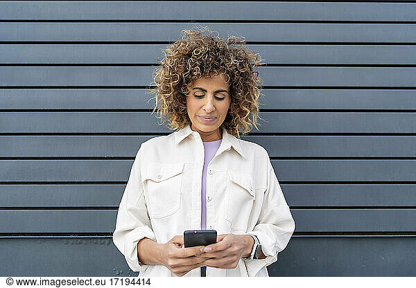 beautiful woman sending a message from her smartphone on a black wall