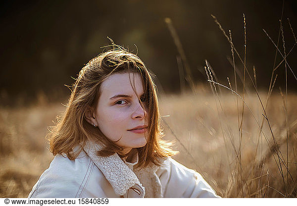 Beautiful woman sitting on soft dry grass during sunset.