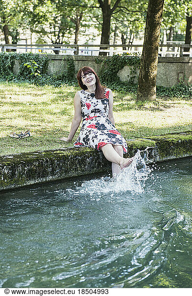 Beautiful woman splashing water with her legs at Eisbach Riverbank