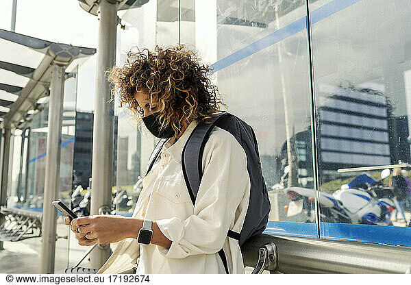 beautiful woman waiting for the bus while looking at her smartphone