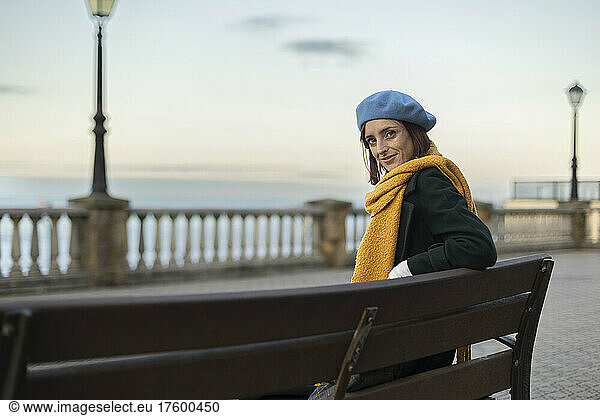 Beautiful woman wearing beret and scarf sitting on bench