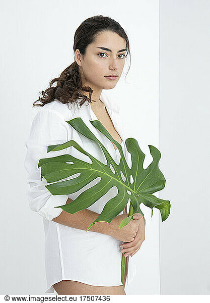 Beautiful woman with blank expression holding monstera leaf
