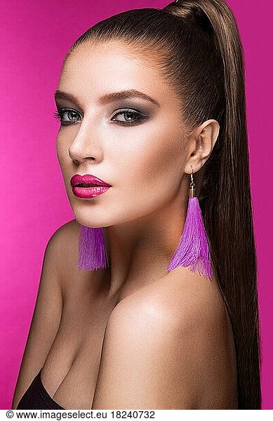 Beautiful woman with evening make-up  bright accessories and long straight hair  Smoky eyes. Fashion photo. Picture taken in the studio on a pink background