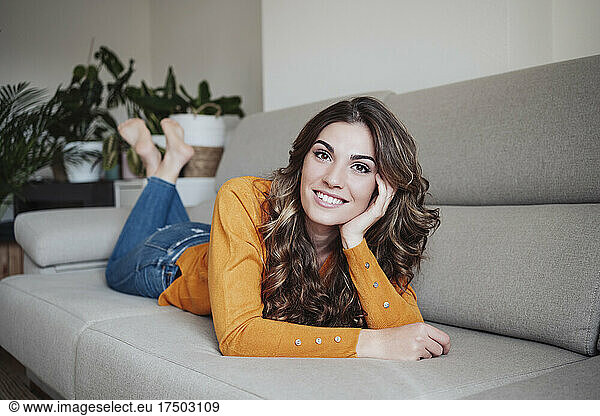 Beautiful woman with wavy hair lying on sofa at home