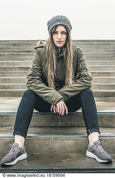 Beautiful young woman in fashionable casual clothes sits on step