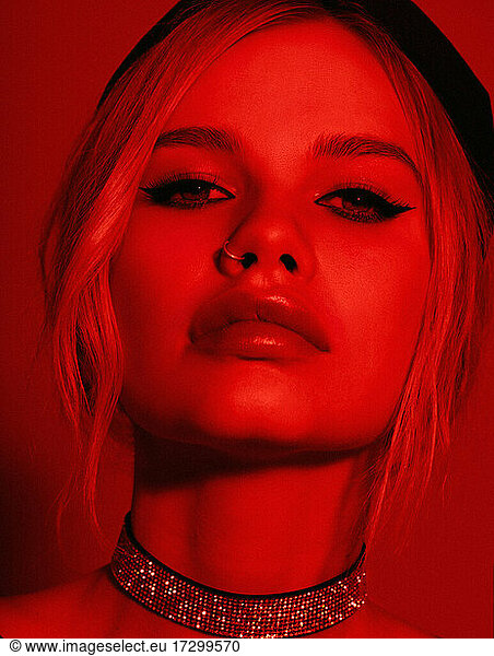 Beauty fashion portrait with red lighting filter. Beauty girl face close up. Closeup blonde woman with dark liner eyes and black hat. neon light red color. stylish fashion portrait art - imag