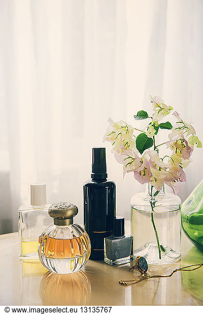 Beauty products with jewelry by flower vase arranged on table