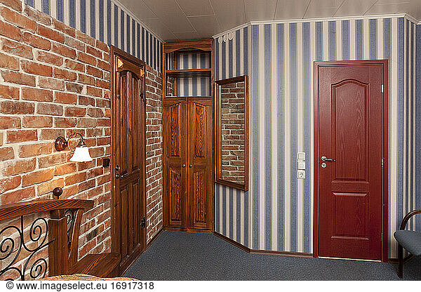 Bed in bedroom with wallpaper and brick wall and wooden cupboards and doors.