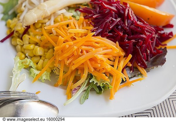 Beet salad with carrot and corn on white plate.