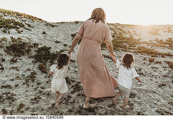 Behind view of mother walking toddler twins in sand to go to the ocean