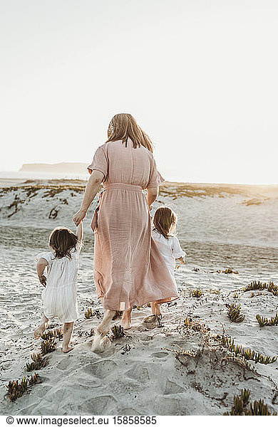 Behind view of mother walking with toddler girl twins to ocean
