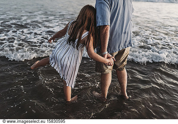 Behind view of red headed daughter holding father's hand in ocean