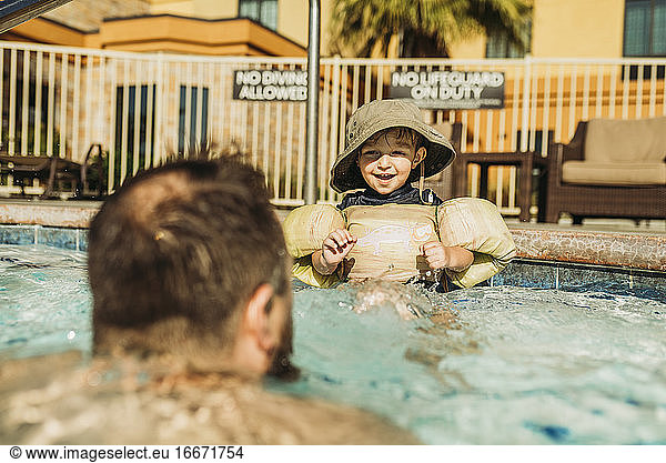 Behind view of young boy playing with dad in water in vacation pool