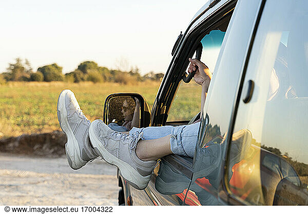 Beine einer jungen Frau am Autofenster bei Sonnenuntergang