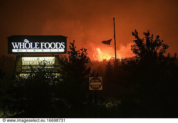 Beleuchtete Schilder mit Waldbrand im Hintergrund bei Nacht